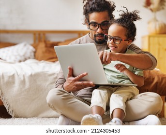 Happy african american family little boy son with young dad watching funny videos on laptop together at home, father with child using computer in bedroom while enjoying weekend - Powered by Shutterstock