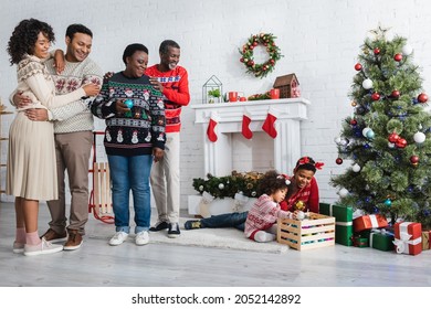 Happy African American Family Looking At Brother And Sister Playing Near Christmas Tree In Living Room