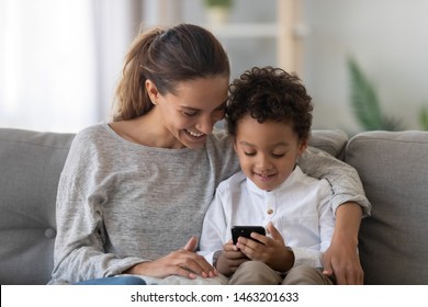 Happy African American Family Mixed Ethnicity Mom Baby Sitter And Cute Little Kid Child Son Having Fun Learning Using Smart Phone Mobile Apps With Mum Control Playing Games On Cellphone At Home