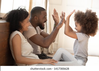 Happy African American Family Mom Dad And Little Cute Kid Girl Having Fun At Home, Mixed Race Small Child Daughter Give High Five To Daddy Play With Parents Laugh Enjoy Warm Moments In The Morning