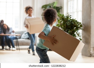 Happy African American Family Moving In New House, Toddler Boy Carrying Cardboard Box, Playing With Preschooler Sister, Mother And Father Sitting On Couch, Looking At Children, Rear View, Close Up