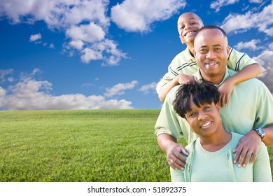 Happy African American Family Over Grass Field, Clouds And Blue Sky - Room For Your Own Text To The Left.