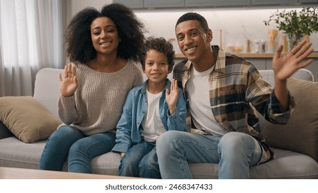 Happy African American family portrait ethnic millennial parents hands male man father mother woman female sit together child little boy son kid waving hands goodbye greet hello look camera sofa home