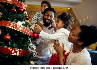 Happy African American family preparing for holidays and decorating Christmas tree at home. Focus is on girl.  - Powered by Shutterstock