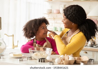 Happy African American Family Preparing Pastry And Having Fun In Kitchen Together. Young Black Mother And Her Little Daughter Enjoying Making Homemade Food, Loving Mom Playfully Touching Child's Nose