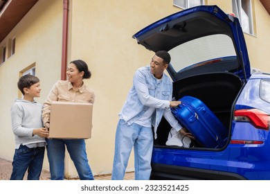 Happy african american family preparing for holiday, putting suitcases and boxes in car trunk, ready to go on vacation trip, child boy helping parents - Powered by Shutterstock