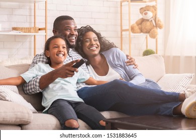 Happy african american family relaxing and watching tv at home, enjoying weekend together.