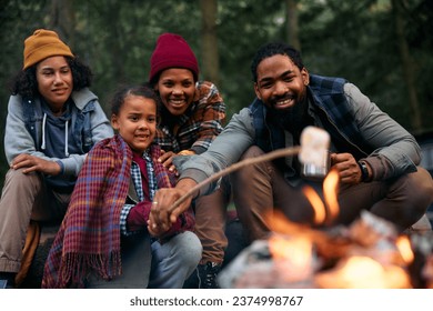 Happy African American family roasting marshmallows while camping in the woods. - Powered by Shutterstock