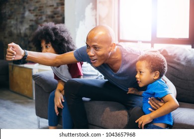 Happy African American Family Of Three Watching Tv And Cheering Sport Games On Sofa At Home