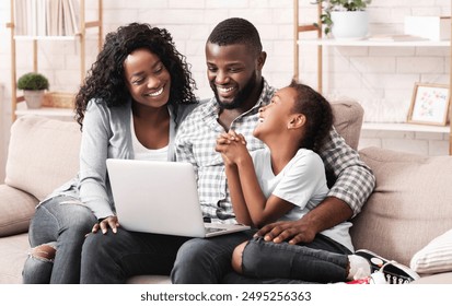 Happy african american family of three watching movie on laptop together, sitting on sofa at home. - Powered by Shutterstock