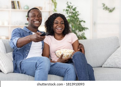Happy african american family of two watching movie together at home, laughing and eating popcorn, copy space