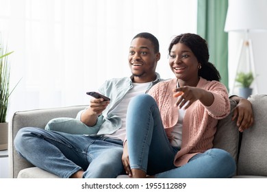 Happy african american family of two watching TV together at home, laughing and hugging, copy space. Joyful black man and woman having fun together on weekend, love and relationships concept