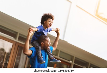 Happy African American Father carrying or piggyback his little son laughing playing and having fun together outside.