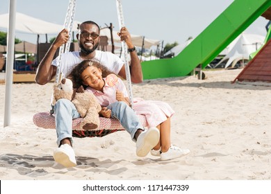 Happy African American Father And Daughter On Spider Web Nest Swing At Amusement Park