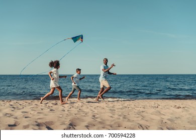 happy african american father and kids playing with kite on beach - Powered by Shutterstock