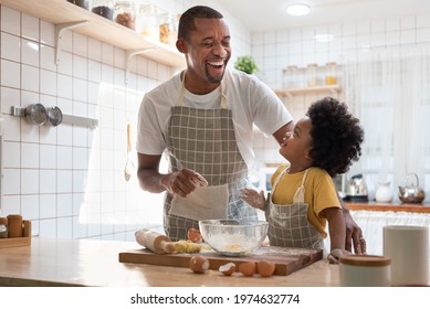 Happy African American Father and little son smiling and laughing while cooking in kitchen. Black family have fun while baking at home - Powered by Shutterstock