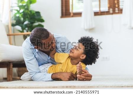 Happy African American Father and little child son playing on the floor at home together, Black family concept.