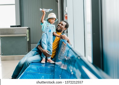 Happy African American Father Looking At Son While Boy Playing With Toy Plane In Airport