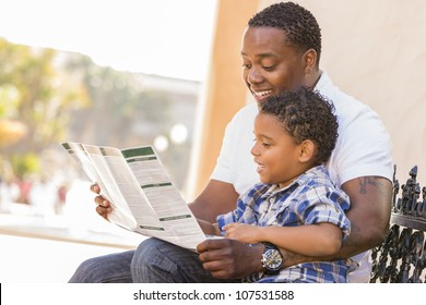 Happy African American Father And Mixed Race Son Having Fun Reading Park Brochure Outside.