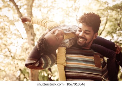 Happy African American Father In Park Carrying His Daughter On Shoulders.