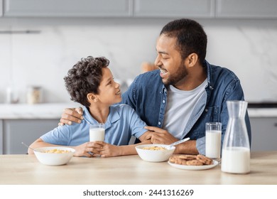 Happy african american father and preteen kid son have breakfast together, drinking milk, eating cereals and cooking. Dad hugging his child, have conversation while eating in kitchen at home - Powered by Shutterstock