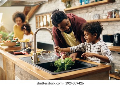 Happy African American father and son washing salad at kitchen sink while making a meal together. Mother and daughter are in the background. - Powered by Shutterstock