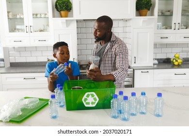 Happy African American Father And Son In Kitchen Talking And Sorting Plastic Waste For Recycling. Family Spending Time At Home.