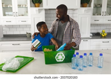 Feliz padre afroamericano e hijo en la cocina hablando y clasificando basura para reciclarse. la familia pasa tiempo en casa.