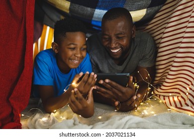 Happy african american father and son lying in blanket fort, using tablet. family spending time at home. - Powered by Shutterstock