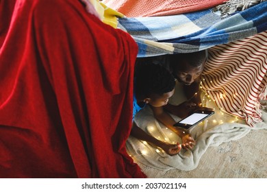 Happy African American Father And Son Lying In Blanket Fort, Using Tablet. Family Spending Time At Home.