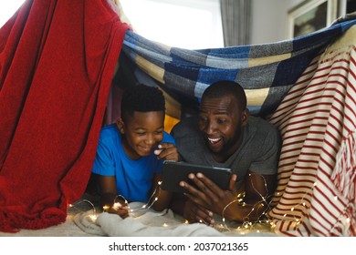 Happy African American Father And Son Lying In Blanket Fort, Using Tablet. Family Spending Time At Home.