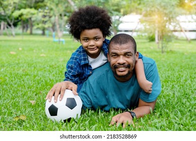 Happy African American Father And Son Playing Football In The Park.