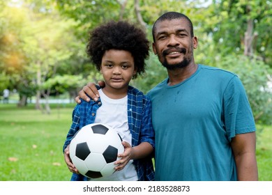 Happy African American Father And Son Playing Football In The Park.