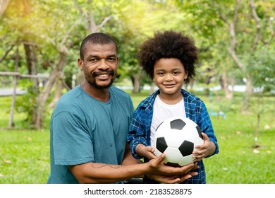 Happy African American Father And Son Playing Football In The Park.