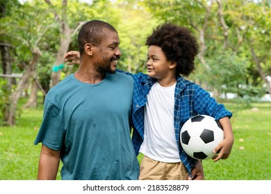 Happy African American Father And Son Playing Football In The Park.