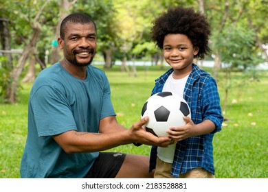 Happy African American Father And Son Playing Football In The Park.