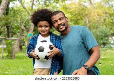 Happy African American Father And Son Playing Football In The Park.