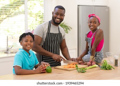 Happy African American Father Teaching Daughter And Son Cooking In The Kitchen. Staying At Home In Isolation During Quarantine Lockdown.