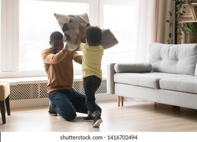 Happy African American father and toddler son playing pillow battle on warm floor at home, smiling black dad with little preschooler child having fun, family funny enjoying activity on weekend - Powered by Shutterstock