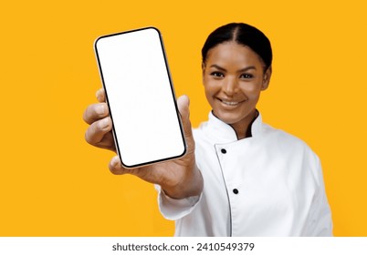 Happy African American Female Chef Showing Blank Smartphone At Camera, Black Smiling Cook Lady Recommending New Mobile App For Food Delivery Order, Standing Over Yellow Background, Mockup - Powered by Shutterstock