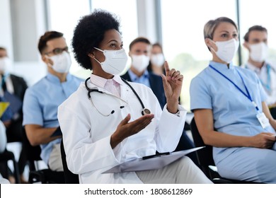 Happy African American Female Doctor With Protective Face Mask Asking A Question While Attending A Seminar In Board Room.