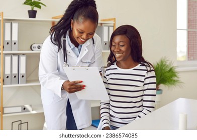 Happy African American female doctor and patient looking at some documents on clipboard. Smiling young woman together with her physician looking at medical report files on clip board - Powered by Shutterstock