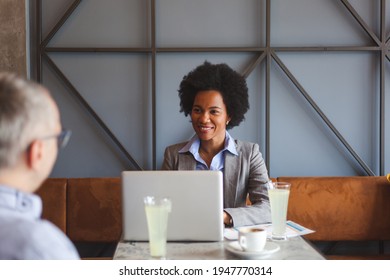 Happy African American female entrepreneur using laptop while communicating with her colleague on a casual meeting in a cafe.