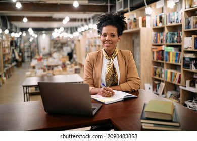 Happy African American Female Professor Holding Online Class From University Library And Looking At Camera. 