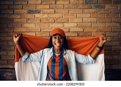 Happy African American Female Sports Fan Holding Flag Of Her Favorite Team During The World Cup And Looking At Camera. Copy Space.