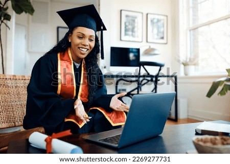 Happy African American female student using laptop and talking during video call after graduation ceremony.