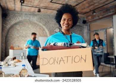 Happy African American female volunteer with donation box with clothes at charity center looking at camera. - Powered by Shutterstock