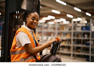 Happy African American female warehouse worker driving pallet jack and looking at camera. - Powered by Shutterstock