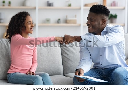 Happy african american girl giving psychotherapist fist bump, clinic interior, child therapy session concept. Black girl teenager having appointment with young man psychologist, celebrating success