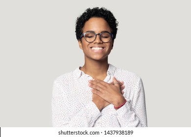 Happy african American girl in glasses isolated on grey studio background keep hands at chest at heart feel grateful, thankful biracial young woman with eyes closed smiling thanking god. Faith concept - Shutterstock ID 1437938189
